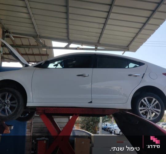 רכב לבן על מעלית במוסך עם מכסה מנוע פתוח